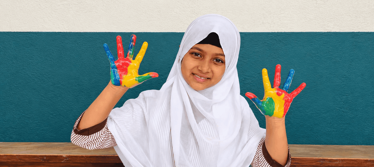 A smiling student of The Progress Academy holding up her paint-covered hands